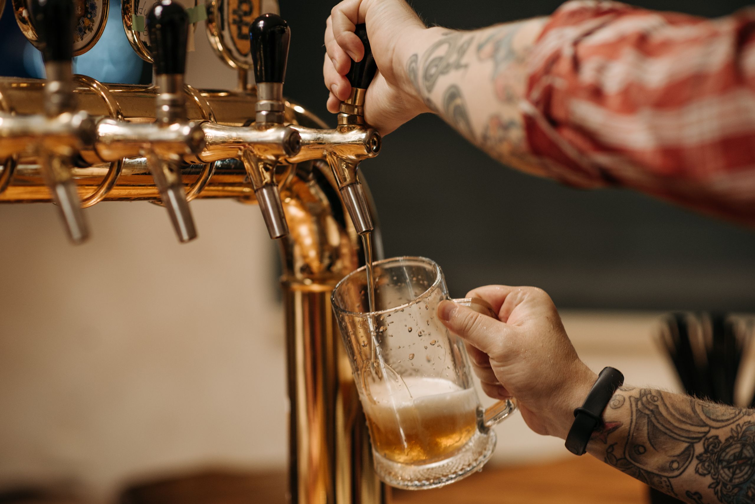 Karriere 2 Tattooed bartender pouring a pint of beer from a golden tap, close-up view at a bar.